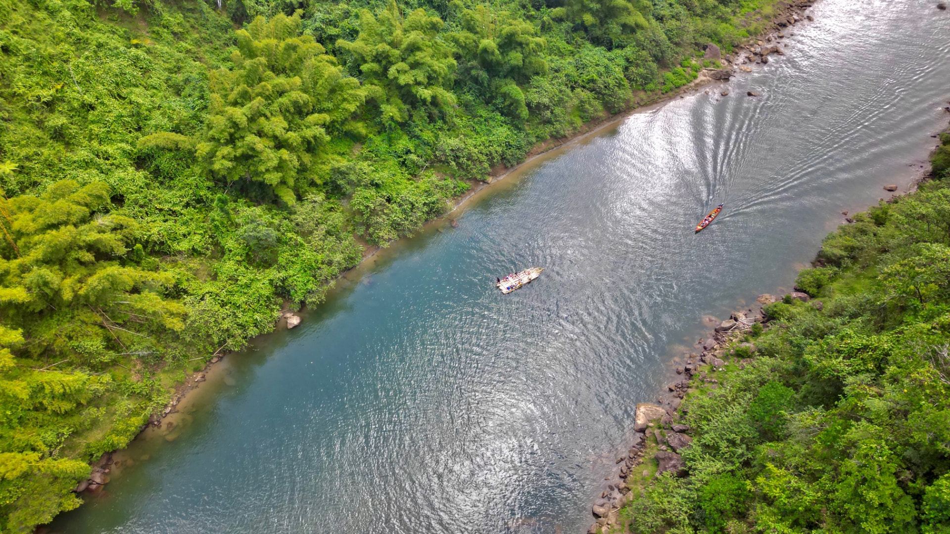 Aerial view of a bamboo bilibili raft and longboat drifting down the rainforest-lined Navua River in Fiji